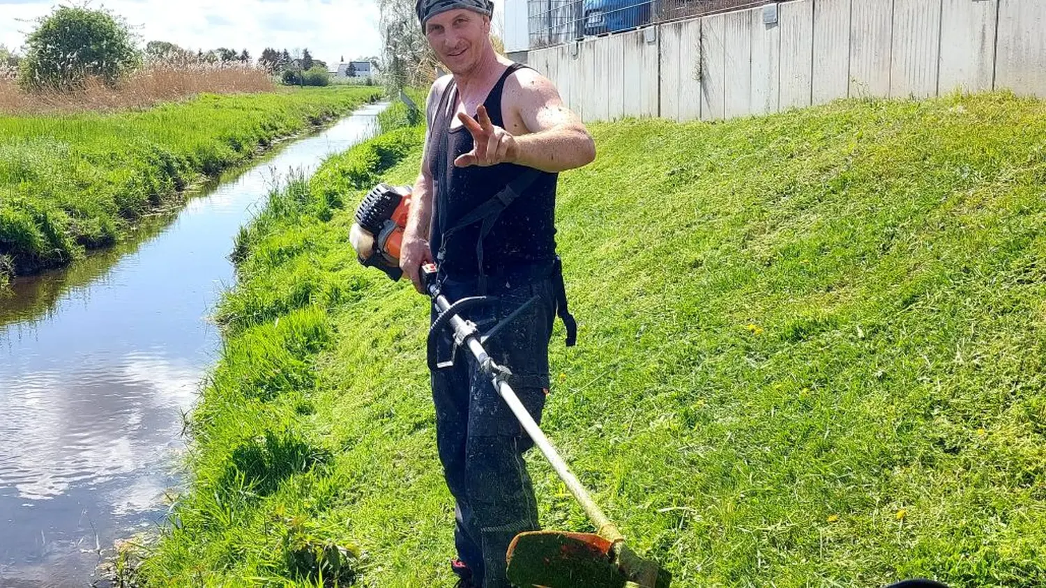 AM Dienstleistung - ein Mann steht am See und trägt die Grasschneidemaschine